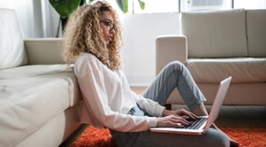 Una mujer crespa, trabajando en su computador portátil, sentada en la alfombra de su casa.