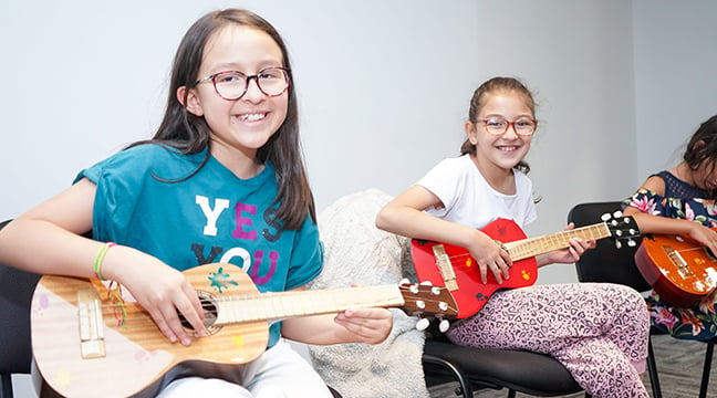 Dos niñas sonriendo y tocando un instrumento de cuerdas