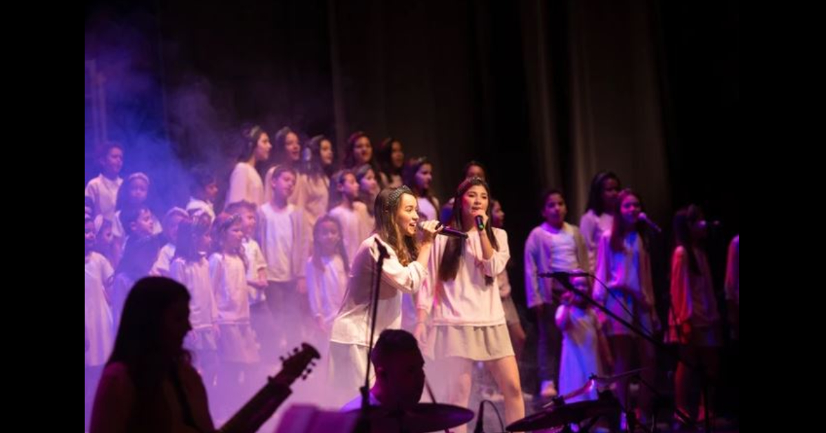 Un grupo de niños y niñas vestidos de blanco cantando en un coro en el teatro Colsubsidio. 