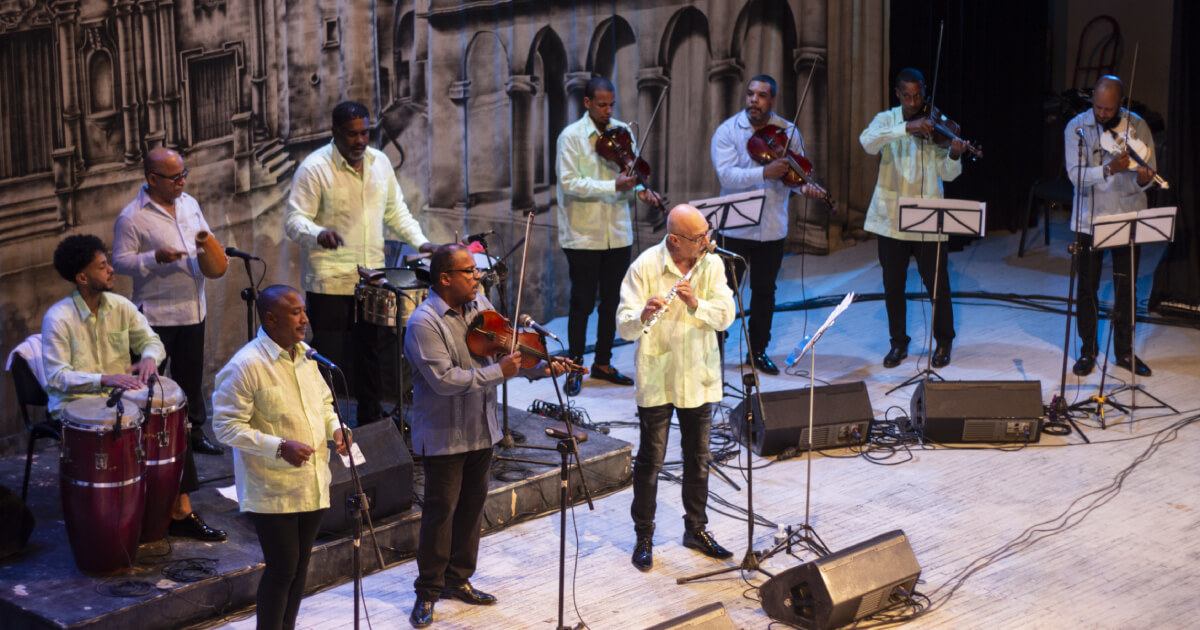 Integrantes de la Orquesta Aragón en concierto, tocando violines, batería y tambores. 