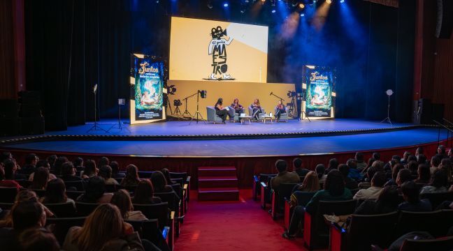Cuatro personas sentadas en sillones participando en un conversatorio sobre un escenario iluminado.