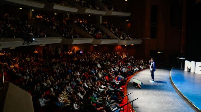 Hombre dando una conferencia en un escenario frente a un auditorio lleno.