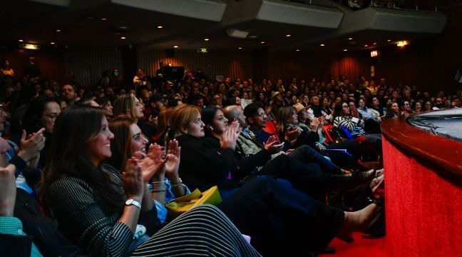 Público en un teatro aplaudiendo con entusiasmo durante una presentación.