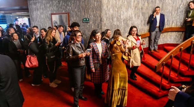 Asistentes conversando en el lobby de alfombra roja de un teatro durante un intermedio.