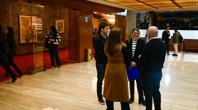 Grupo de personas conversando en el vestíbulo de un centro cultural o teatro.